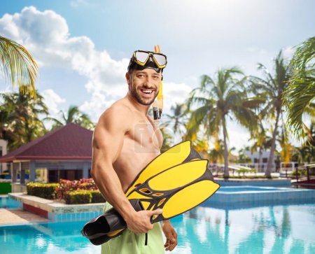 Foto de Joven en traje de baño con una máscara de buceo sosteniendo aletas de snorkel junto a una piscina - Imagen libre de derechos