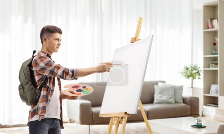 Téléchargez les photos : Homme étudiant peignant sur une toile dans un appartement - en image libre de droit