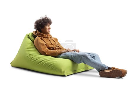 Foto de Gen z chico sentado en una silla bolsa de frijol verde y sonriendo aislado sobre fondo blanco - Imagen libre de derechos