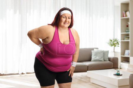 Téléchargez les photos : Femme de taille plus en vêtements de sport avec un dos raide debout à la maison dans un salon - en image libre de droit
