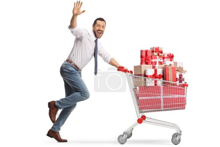 Foto de Emocionado hombre de negocios corriendo con regalos en un carrito de compras y saludando a la cámara aislada sobre fondo blanco - Imagen libre de derechos