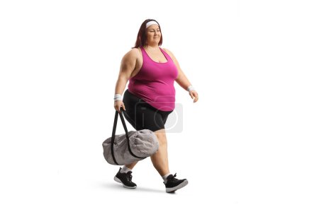 Téléchargez les photos : Plan complet d'une femme de taille plus en vêtements de sport marchant et portant un sac de sport isolé sur fond blanc - en image libre de droit
