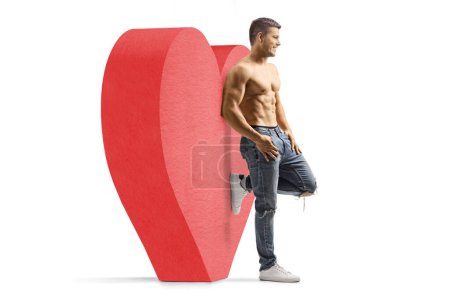 Photo for Full length profile shot of a shirtless guy wearing jeans and leaning on a red heart isolated on white background - Royalty Free Image