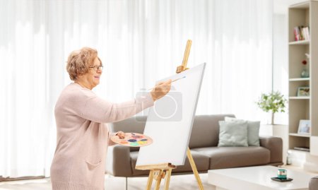 Photo for Elderly woman painting on a canvas in an apartment - Royalty Free Image