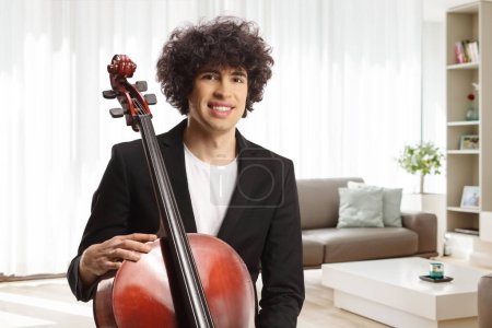 Foto de Retrato de un joven artista masculino con un violonchelo posando en casa en una sala de estar - Imagen libre de derechos