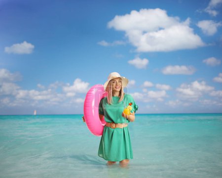 Téléchargez les photos : Jeune femme avec un anneau de natation debout dans la mer des Caraïbes et tenant un cocktail - en image libre de droit