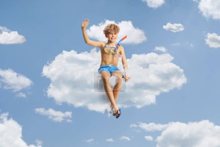Foto de Niño en pantalones cortos de natación y una máscara de buceo sentado en una nube y saludando - Imagen libre de derechos