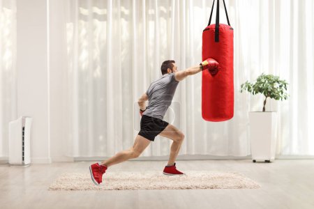 Foto de Hombre fuerte golpeando una bolsa de boxeo en casa - Imagen libre de derechos