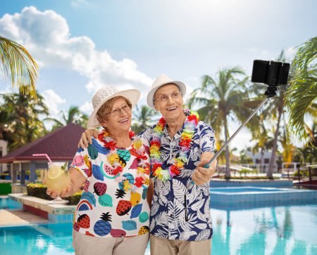 Téléchargez les photos : Touristes âgés prenant un selfie avec un bâton près d'une piscine - en image libre de droit