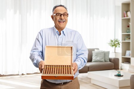 Photo for Mature man with a box of cuban cigars standing in a living room at home - Royalty Free Image