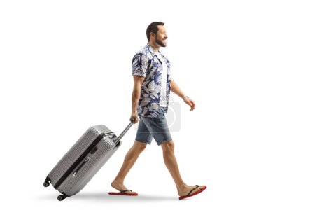 Photo for Man in flip-flops pulling a suitcase smiling and walking isolated on white background - Royalty Free Image
