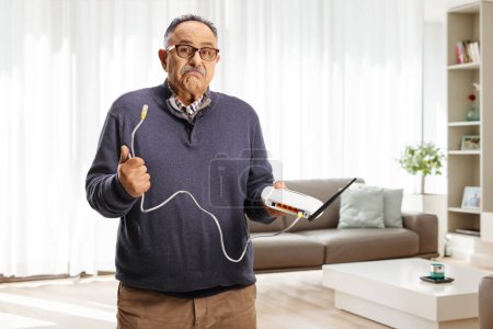 Téléchargez les photos : Homme mature confus tenant un câble de routeur dans un salon - en image libre de droit