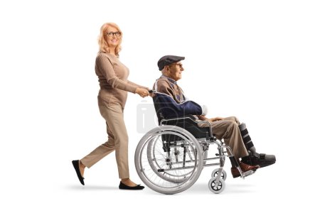 Foto de Mujer de mediana edad empujando a un anciano con un brazo roto en una silla de ruedas aislada sobre fondo blanco - Imagen libre de derechos