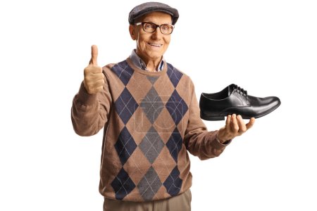 Foto de Hombre mayor sosteniendo un zapato de cuero negro y haciendo gestos con los pulgares hacia arriba aislado sobre fondo blanco - Imagen libre de derechos