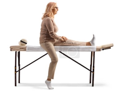 Téléchargez les photos : Plan de profil complet d'une femme assise sur une table de physiothérapie isolée sur fond blanc - en image libre de droit