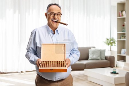 Foto de Hombre maduro fumando un cigarro en casa y sosteniendo una caja de puros - Imagen libre de derechos