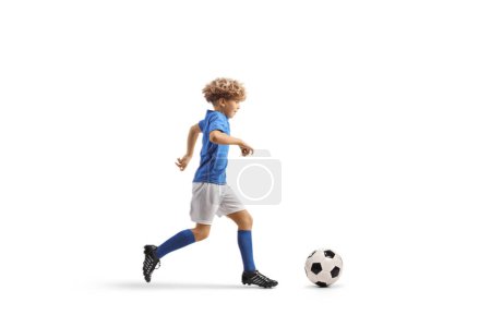 Foto de Tiro de perfil completo de un niño en un kit de fútbol corriendo y liderando una pelota aislada sobre fondo blanco - Imagen libre de derechos