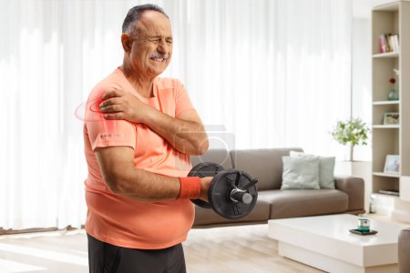 Téléchargez les photos : Homme mûr avec épaule douloureuse faisant de l'exercice avec des poids à la maison - en image libre de droit