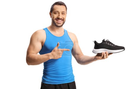 Téléchargez les photos : Athlète masculin tenant une chaussure de sport d'entraîneur et pointant isolé sur fond blanc - en image libre de droit