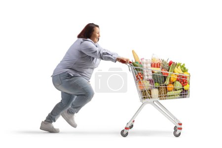 Photo for Full length profile shot of a plus size female running with food in a shopping cart isolated on white background - Royalty Free Image