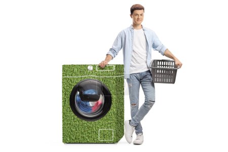 Téléchargez les photos : Un type tenant un panier à linge et se tenant à côté d'une machine à laver verte isolée sur fond blanc - en image libre de droit