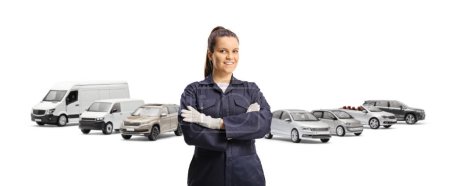 Photo for Young female mechanic worker in an overall uniform and gloves posing in front of parked vehicles isolated on white background - Royalty Free Image