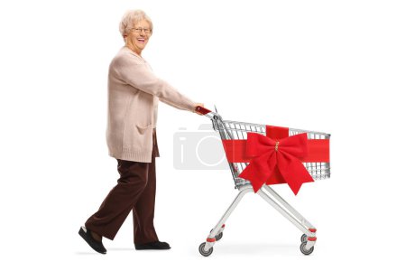 Téléchargez les photos : Plan complet d'une femme âgée poussant un chariot vide avec ruban rouge arc isolé sur fond blanc - en image libre de droit