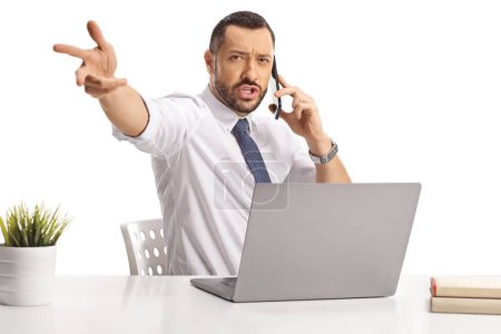 Photo for Angry businessman using a smartphone sitting at a desk with laptop and throwing something isolated on white background - Royalty Free Image