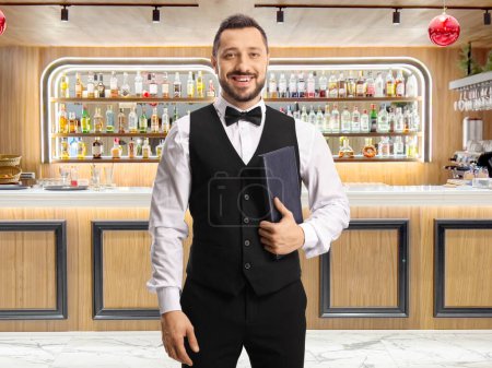 Photo for Waiter with a bow tie holding a menu list in a luxury hotel at the bar - Royalty Free Image
