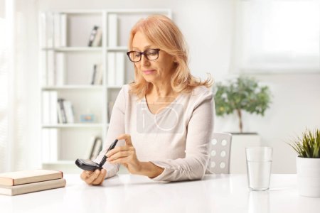 Téléchargez les photos : Femme d'âge moyen avec moniteur de glucose vérifiant le niveau d'insuline à la maison - en image libre de droit
