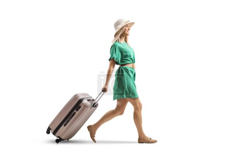 Foto de Mujer joven en un vestido verde caminando y tirando de una maleta aislada sobre fondo blanco - Imagen libre de derechos