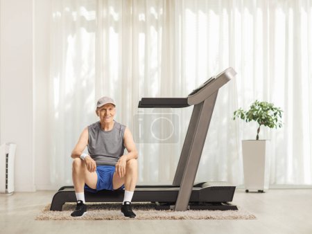 Foto de Anciano sentado en una cinta de correr en casa - Imagen libre de derechos
