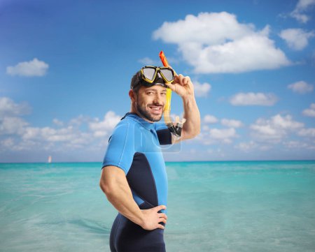 Téléchargez les photos : Jeune homme en combinaison de plongée et masque marchant dans une mer bleu cristal - en image libre de droit