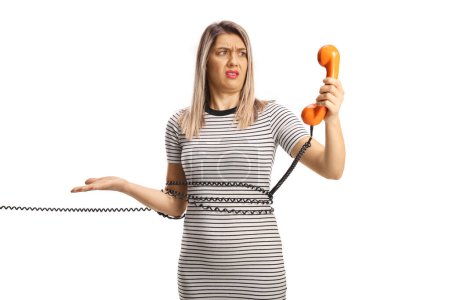 Photo for Angry woman tied with a cable from a vintage rotary phone looking at the handset isolated on white background - Royalty Free Image