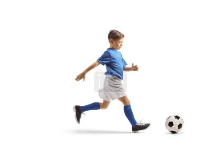 Téléchargez les photos : Garçon dans un kit de football bleu et blanc courir rapidement avec et diriger une balle isolée sur fond blanc - en image libre de droit