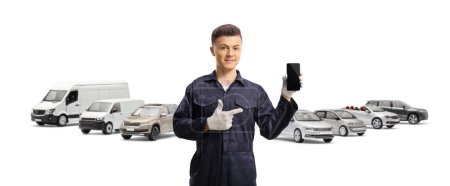 Photo for Young mechanic at a parking lot holding a mobile phone and pointing isolated on white background - Royalty Free Image