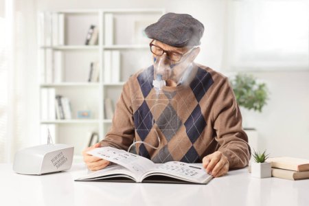 Téléchargez les photos : Homme âgé utilisant un nébuliseur et lisant un livre à la maison à une table - en image libre de droit