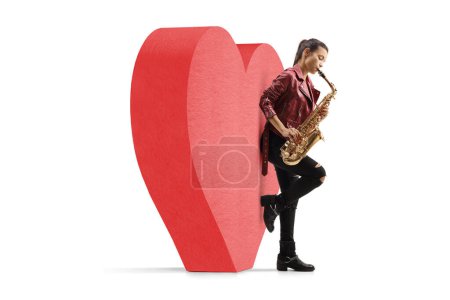 Photo for Young woman playing saxophone and leaning on a red heart, love and romance concept isolated on white background - Royalty Free Image