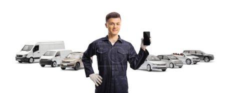 Téléchargez les photos : Jeune mécanicien tenant un téléphone portable devant des véhicules garés isolés sur fond blanc - en image libre de droit