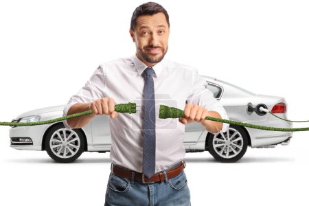 Foto de Hombre sosteniendo cables verdes frente a un coche eléctrico aislado sobre fondo blanco, concepto de energía sostenible - Imagen libre de derechos