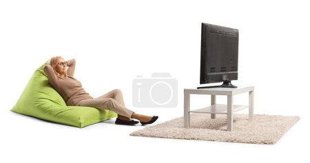 Téléchargez les photos : Femme d'âge moyen sur un fauteuil sac haricot vert regarder la télévision isolé sur fond blanc - en image libre de droit