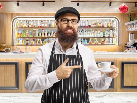 Photo for Waiter with an apron holding an espresso coffee and pointing in front of a bar - Royalty Free Image