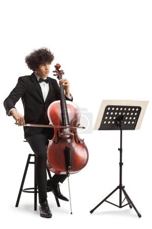 Photo for Young male musician performing with a cello and looking at a music note stand isolated on white background - Royalty Free Image