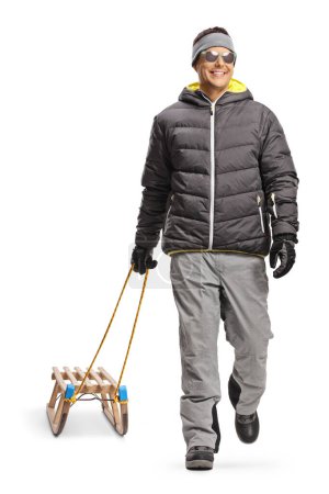 Téléchargez les photos : Portrait d'un homme vêtu d'une veste d'hiver marchant et tirant un traîneau en bois isolé sur fond blanc - en image libre de droit