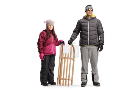 Foto de Padre e hija en ropa de invierno de pie con un trineo de madera aislado sobre fondo blanco - Imagen libre de derechos