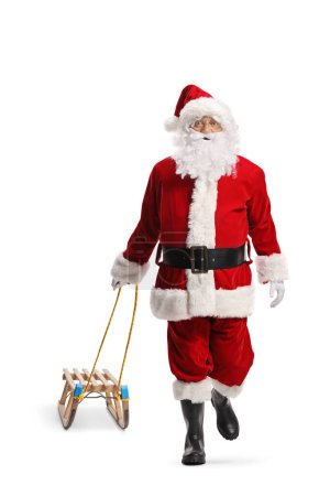 Foto de Santa Claus caminando hacia la cámara y tirando de un trineo de madera aislado sobre fondo blanco - Imagen libre de derechos