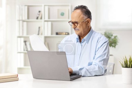 Téléchargez les photos : Homme mûr assis dans un bureau et travaillant sur un ordinateur portable - en image libre de droit