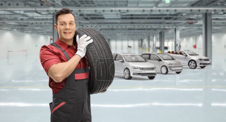 Photo for Mechanic carrying a car tire in a garage - Royalty Free Image
