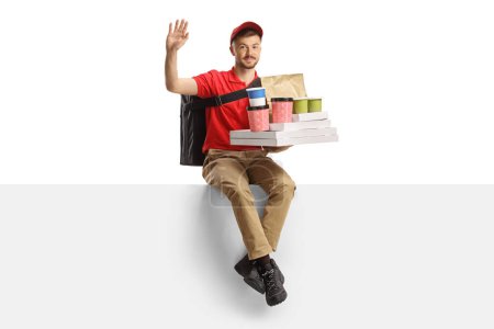 Photo for Food delivery guy with a bag and boxes sitting on a blank panel and waving isolated on white background - Royalty Free Image