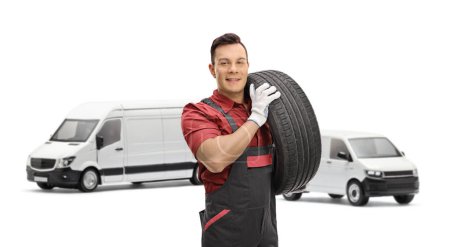 Téléchargez les photos : Mécanicien automobile portant un pneu de fourgon et regardant la caméra isolée sur fond blanc - en image libre de droit